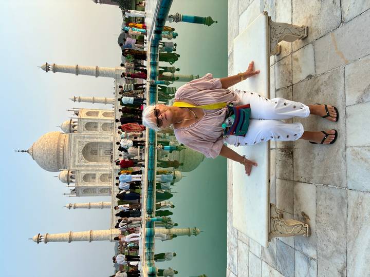 Woman sits on a marble bench in front of the Taj Mahal with reflections in the water behind her.