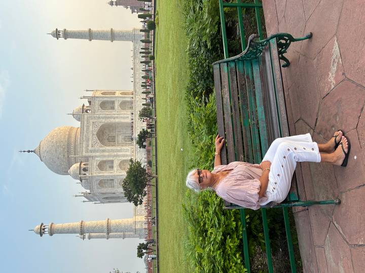 Woman on a green park bench with the Taj Mahal looming majestically in the background.