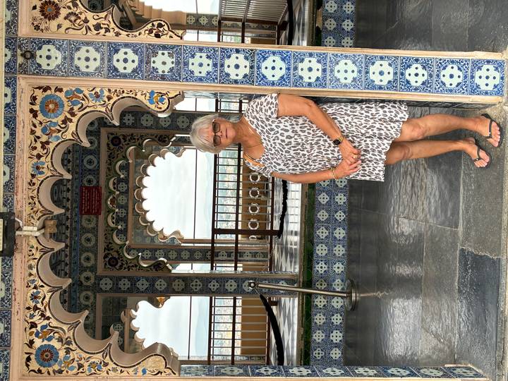Woman stands in front of ornate blue and white tiled arches inside an Indian palace.