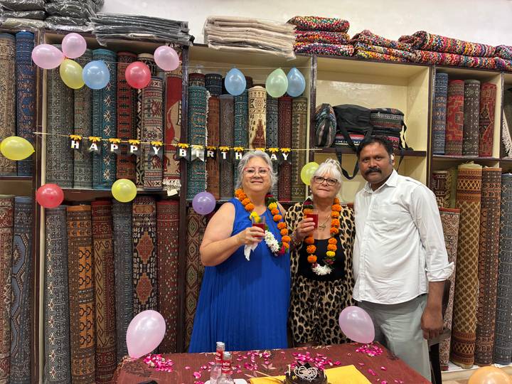 Birthday celebration inside a carpet shop with balloons and garlands, three people posing and smiling.