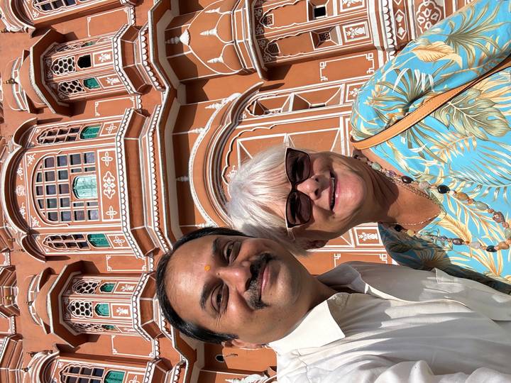 Selfie of a guide and tourist smiling in front of the ornate pink façade of Hawa Mahal.