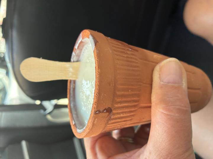 Clay cup of lassi held in a hand with a wooden spoon inside, photographed inside a car.