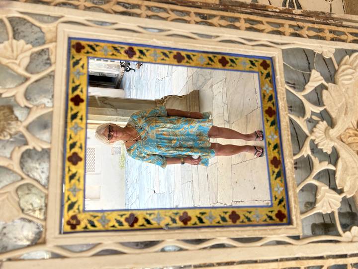 Woman’s full-body reflection in an ornate framed mirror set within marble inlay walls.