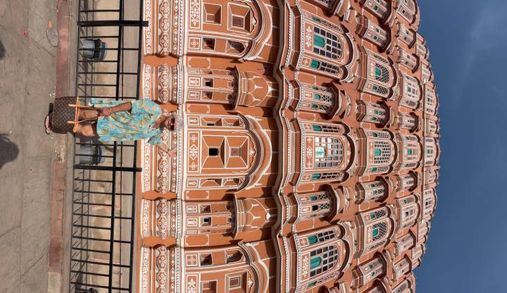 Woman poses in front of the towering façade of Hawa Mahal captured in a vertical panoramic shot.