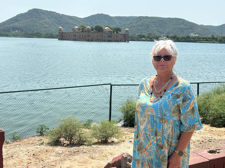 Woman stands beside Man Sagar Lake with Jal Mahal floating palace in the distance.