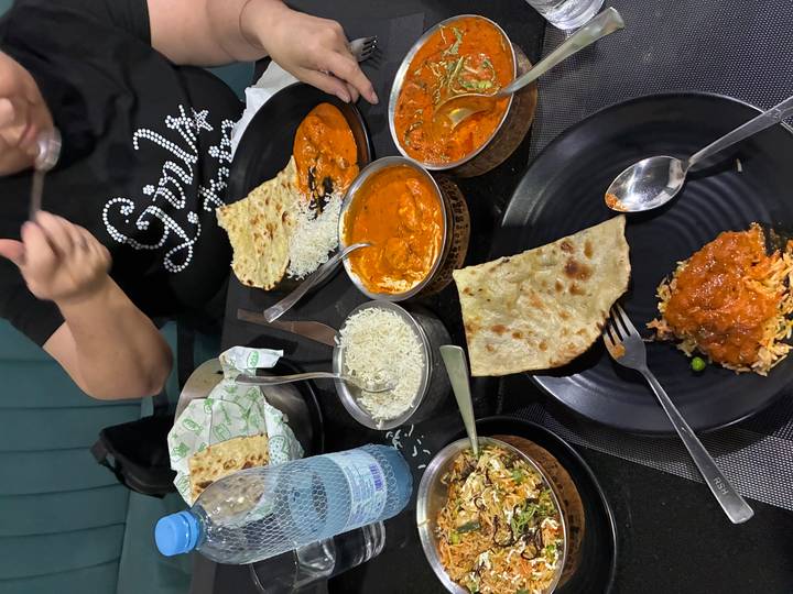 Table filled with Indian curries, naan and rice being enjoyed by diners.