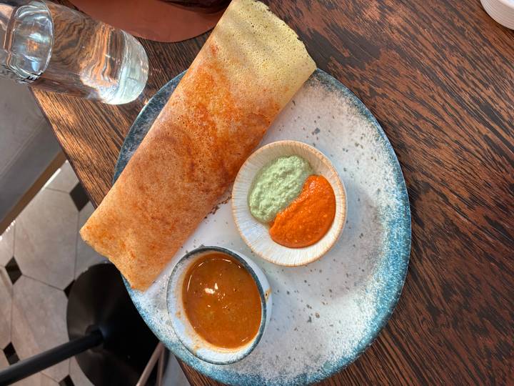 South Indian dosa with bowls of red and green chutney and sambar on a rustic wooden table in bright indoor light.