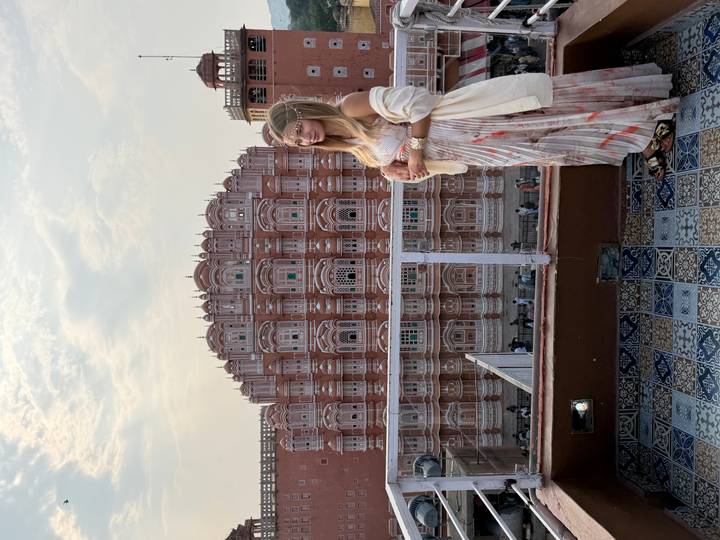 Traveller on rooftop terrace with the ornate pink façade of Hawa Mahal rising behind.