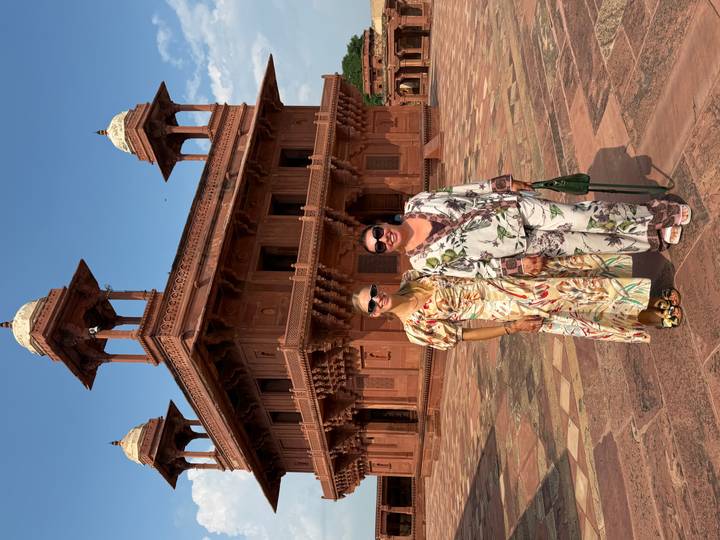 Two women posing in front of red-sandstone palace buildings in Fatehpur Sikri.