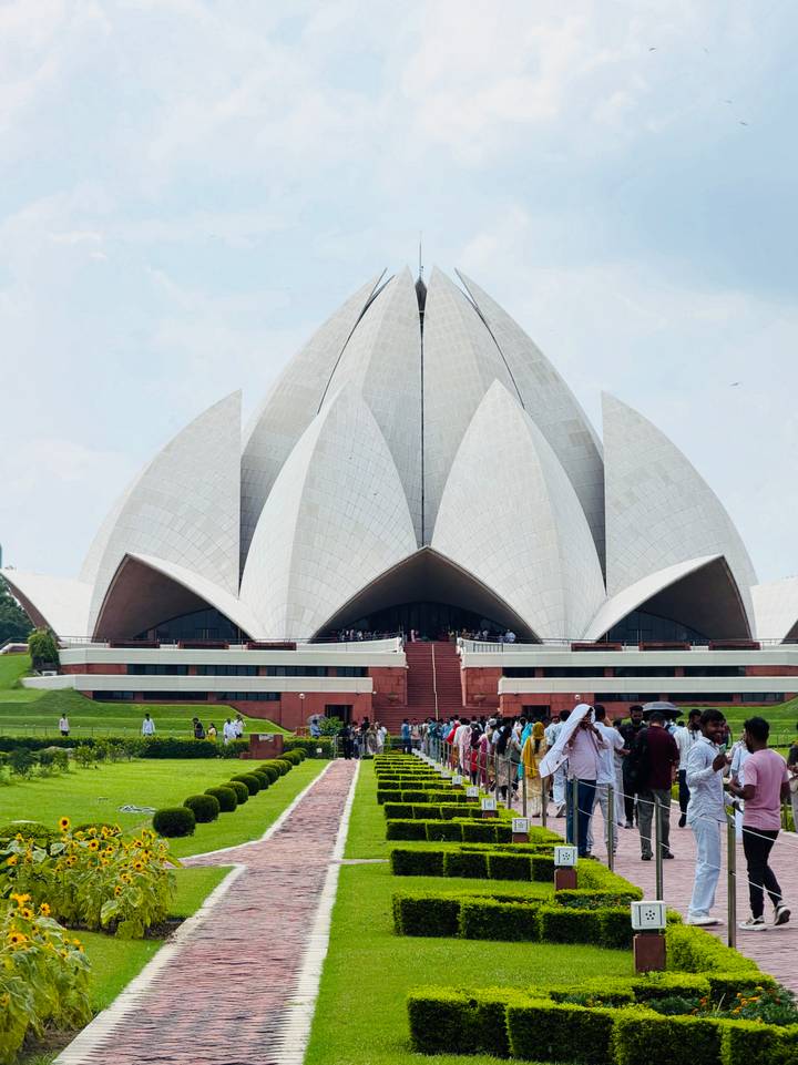The striking white petals of the Lotus Temple with crowds gathered at the base on a bright day.