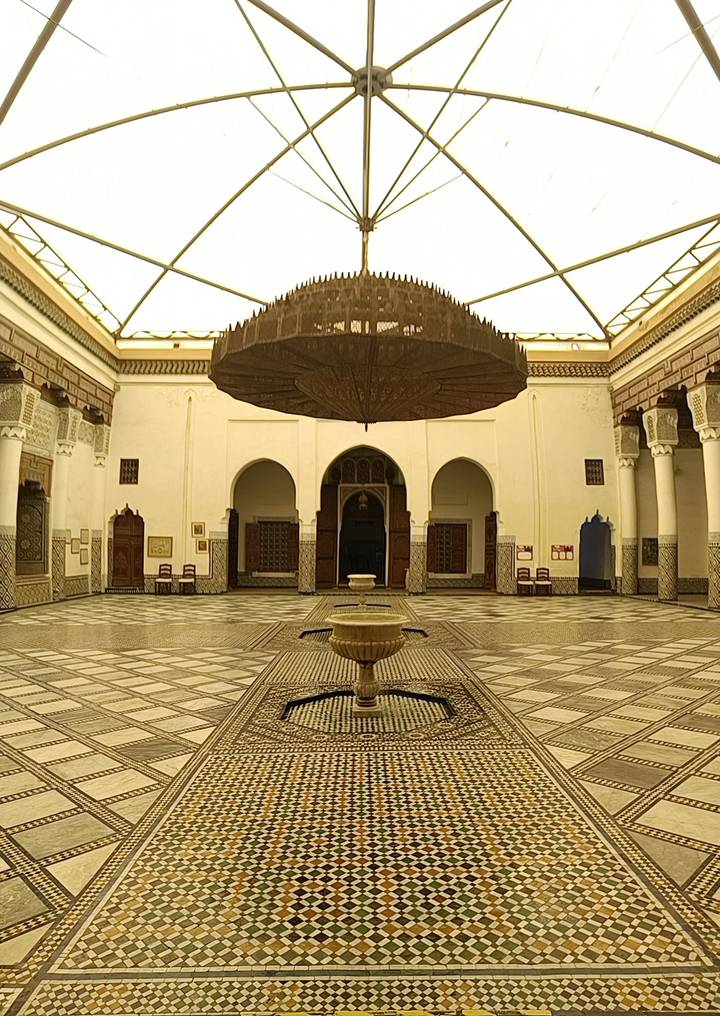Elegant Moroccan courtyard with mosaic floors, arched doorways and a central fountain beneath a grand chandelier.