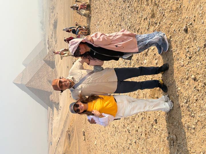 Three tourists pose with camels in front of the hazy pyramids on the Giza Plateau.