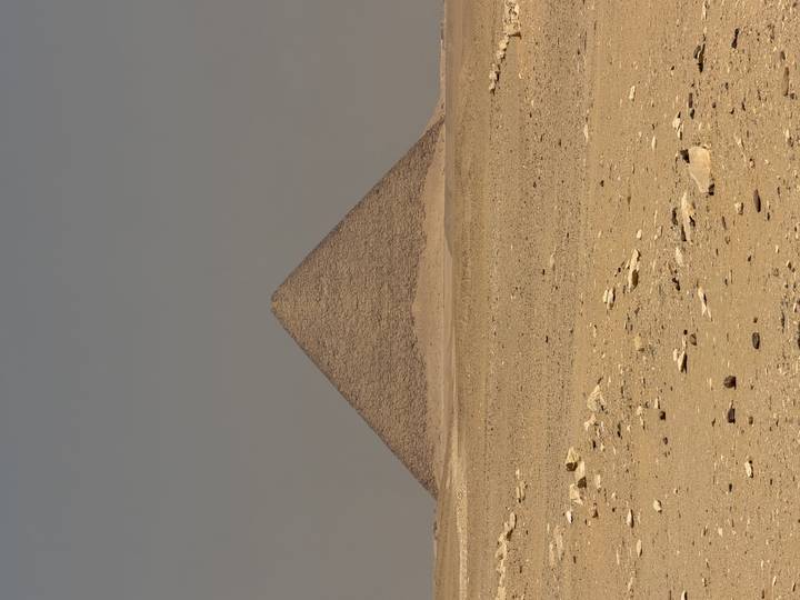 Isolated pyramid rises from the flat, sandy expanse under a muted desert sky.