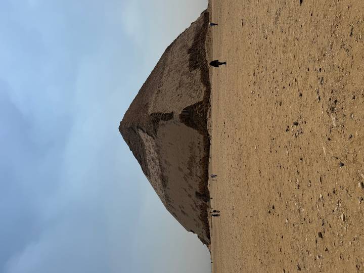 Visitors walk toward the Bent Pyramid whose limestone casing gives a two-angled profile against the sky.