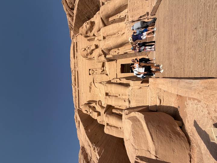 Tourists gather at the colossal seated statues and entrance of Abu Simbel carved into sandstone cliffs.
