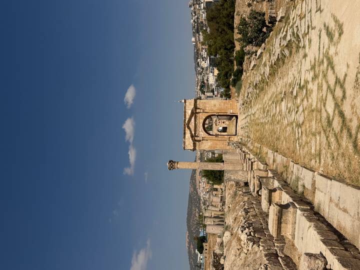 Stone archway and column line the ancient cardo of Jerash with the modern town visible beyond.
