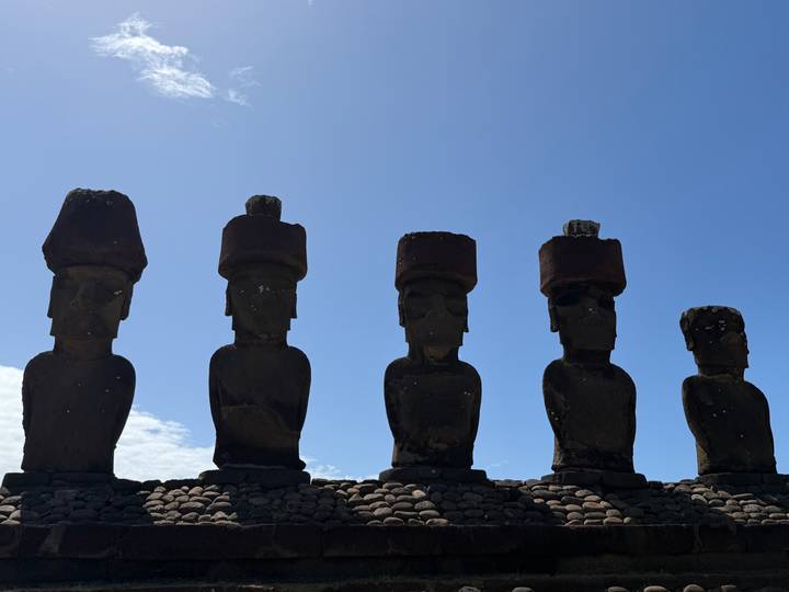 Silhouetted moai with pukao topknots stand in sharp contrast against a bright sky.