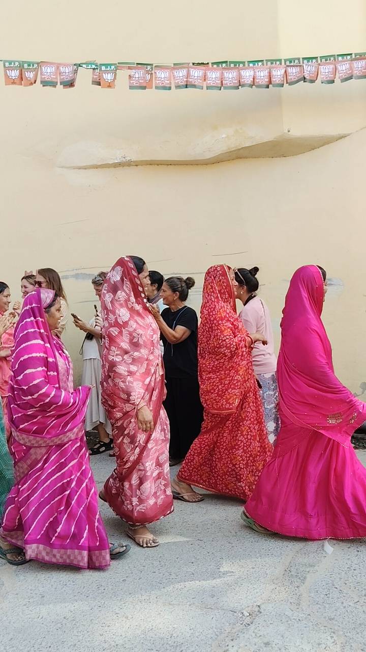 A colorful line of Indian women in patterned saris stand beside foreign visitors during a cultural gathering.