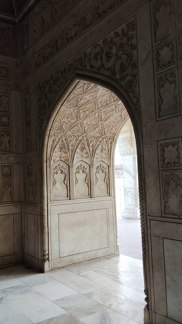 Intricately carved marble archway with floral motifs inside a Mughal monument.