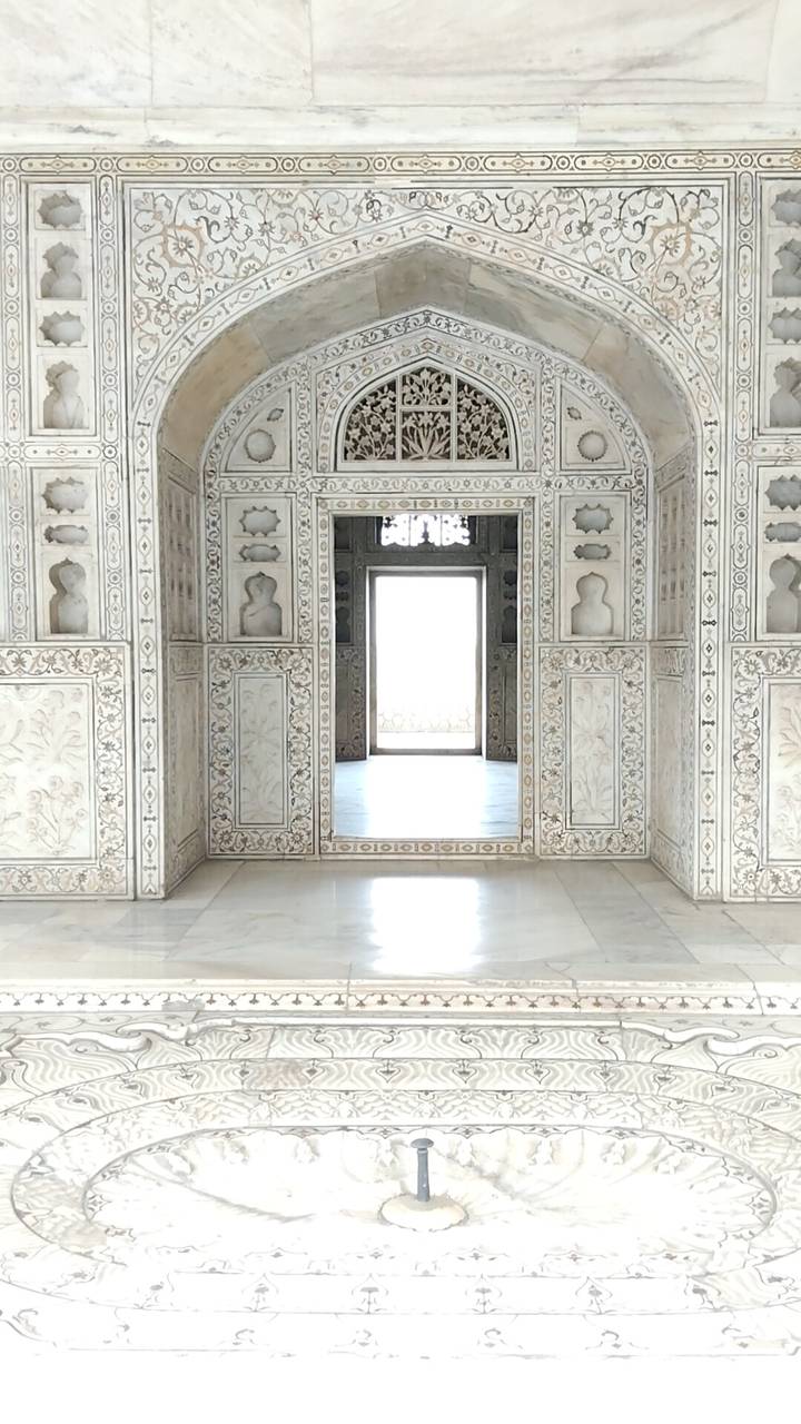 Symmetrical marble chamber with delicate inlay work and a brightly lit doorway at the far end.