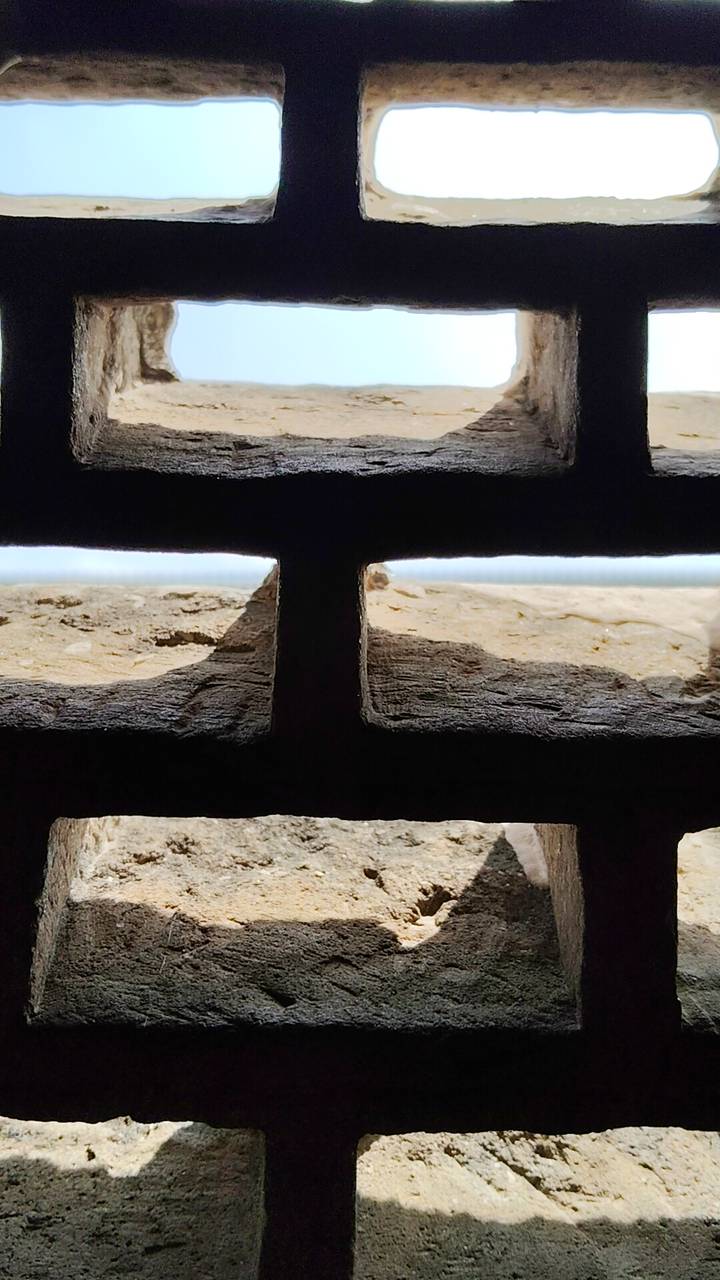 Abstract close-up view through a rough wooden lattice with bright light beyond.