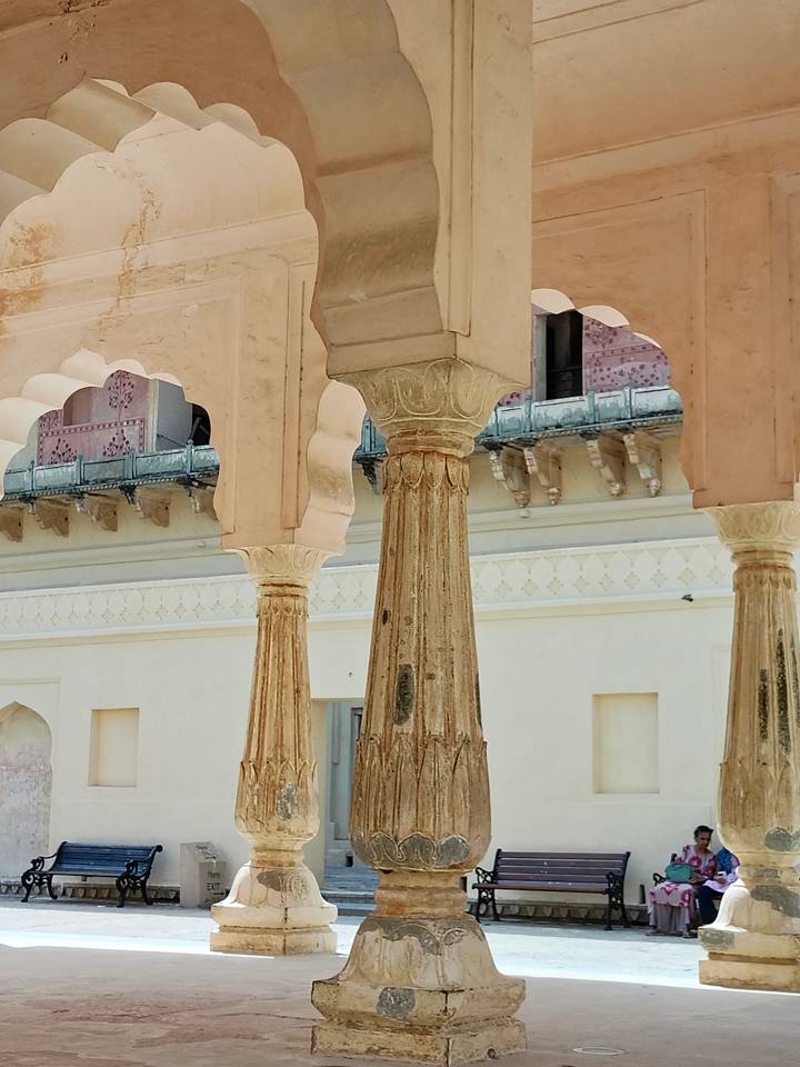 Weathered sandstone columns with intricate capitals inside an Indian palace courtyard.