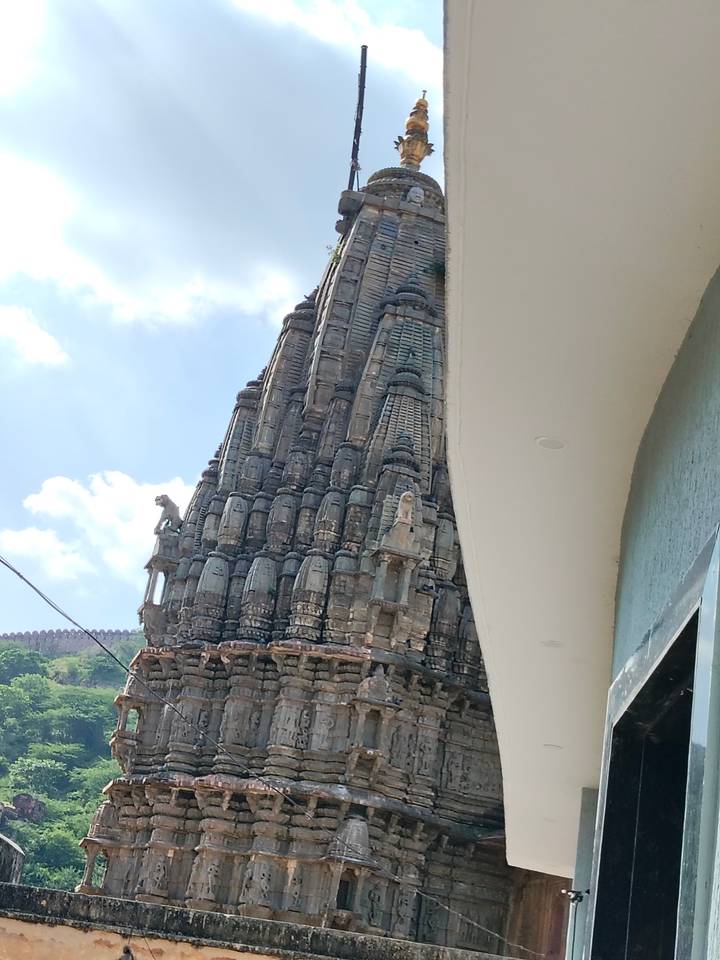 Stone temple spire rises beside a modern white façade under a bright sky.