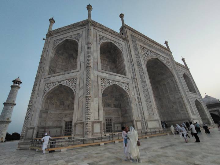 Wide-angle view of the Taj Mahal marble façade at dusk with visitors walking nearby.