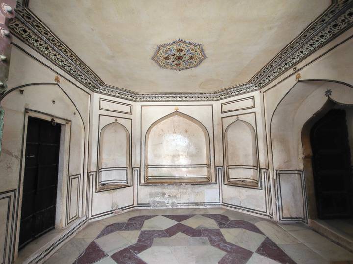 A small octagonal room with faded frescoes, arched niches, and patterned floor tiles.