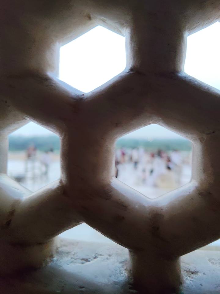 View through a hexagonal marble lattice with blurred crowd and river beyond.
