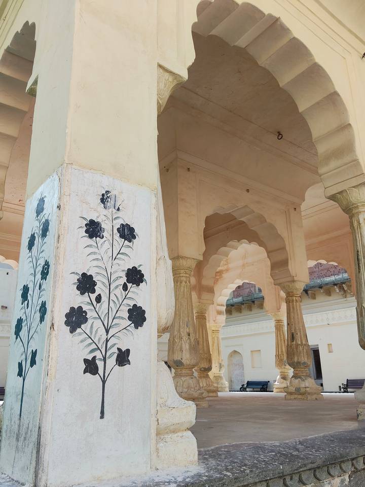 Marble pillar painted with black floral motifs amid scalloped sandstone arches.