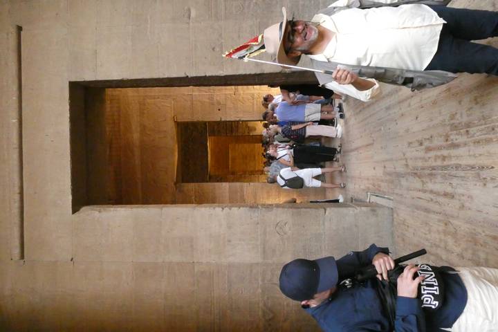 Crowd of tourists moves through a dim sandstone corridor inside an ancient Egyptian temple.