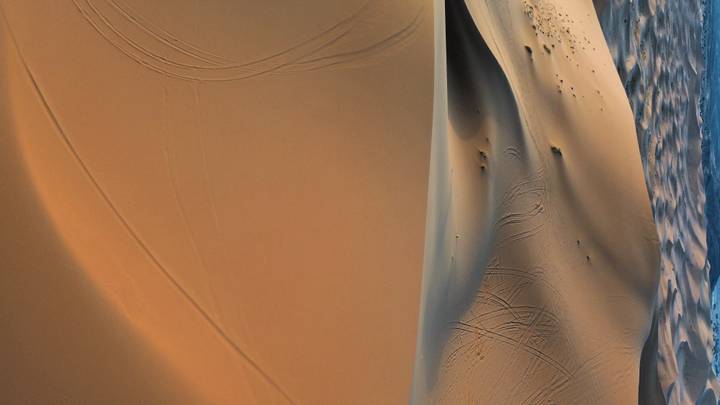Expansive view of smooth orange sand dunes with vehicle track patterns.