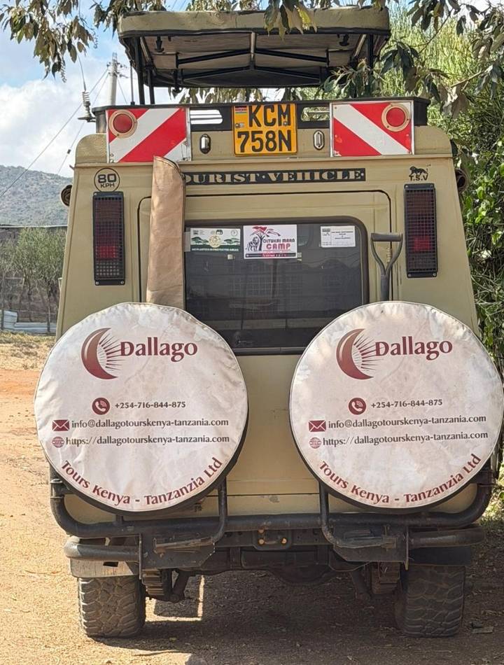 Rear view of a Kenyan safari jeep with company logos and spare-tyre covers parked on dirt