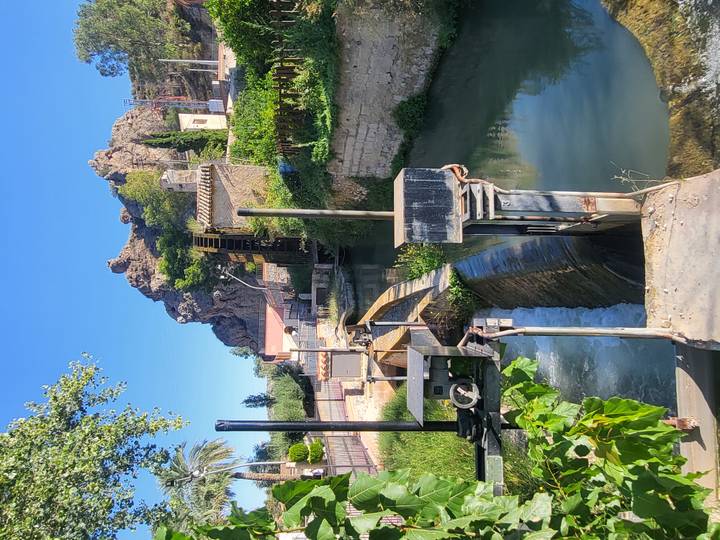 Historic wooden water wheel beside a rocky hill and canal surrounded by greenery in Cieza.