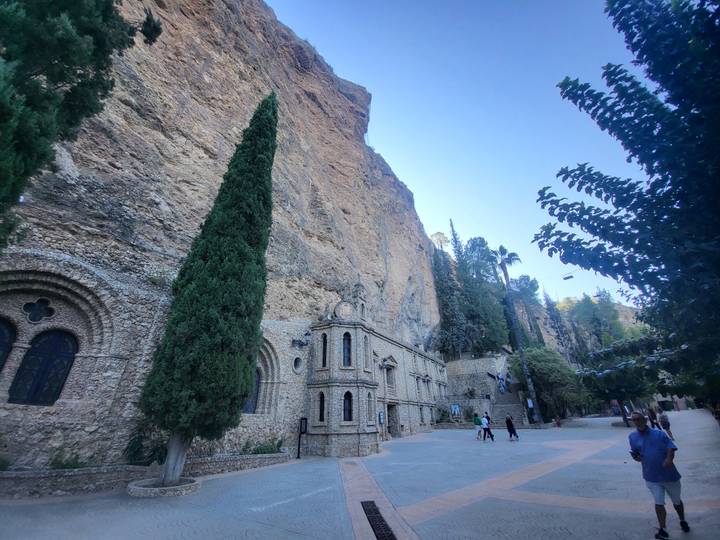 Sanctuary buildings nestle against a towering cliff face amidst tall cypress trees at Calasparra.
