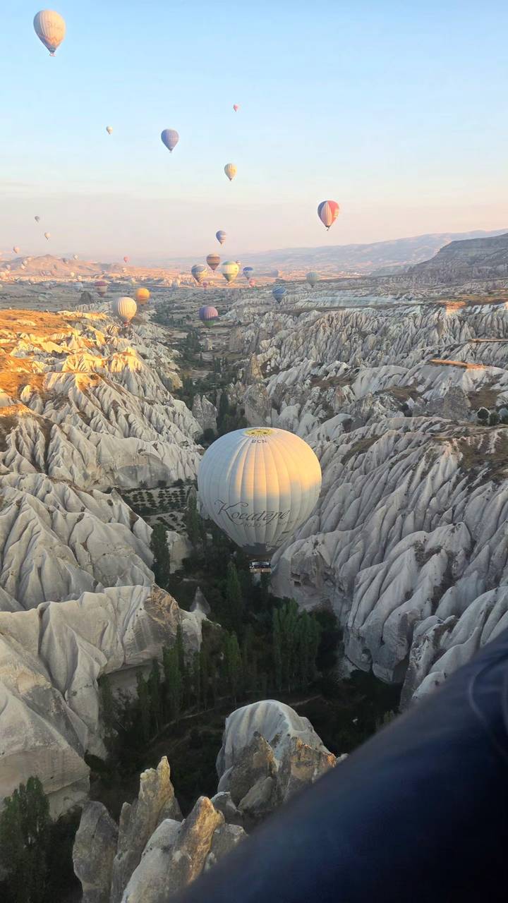 Hot-air balloon drifts through dramatic rock valleys at sunrise in Cappadocia.