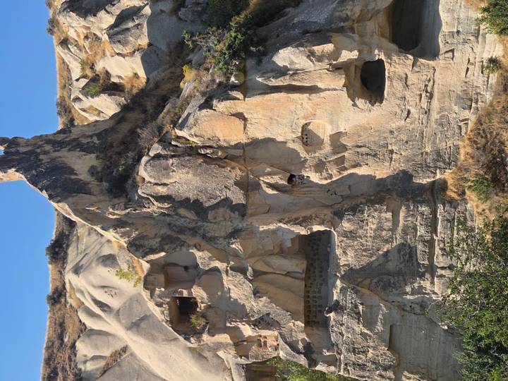 Soft-eroded cliffs with ancient cave dwellings carved into beige rock of Cappadocia.