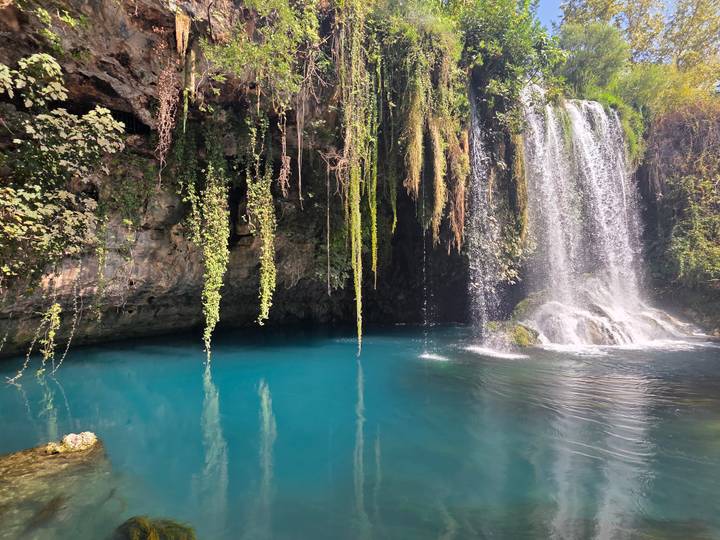 Crystal-blue plunge pool beneath a lush cascading waterfall fringed with hanging vines.