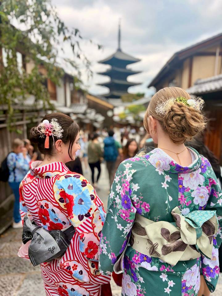 Two women in colorful kimonos admire a historic Kyoto street filled with visitors.