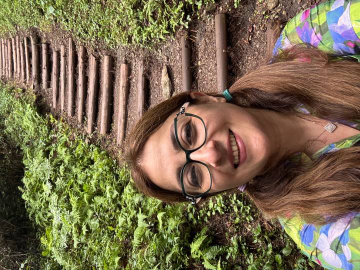 A smiling woman takes a selfie on a lush forest trail beside rustic wooden steps climbing a hill.