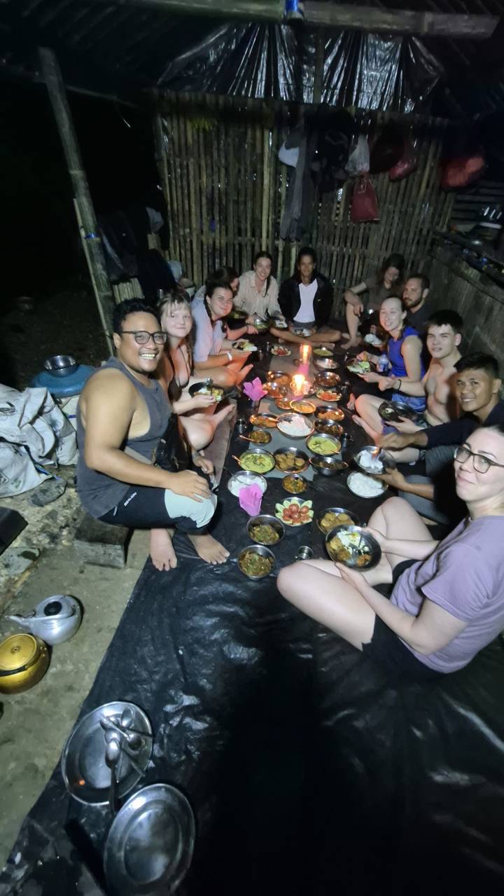 Travellers sit barefoot on ground tarps around a spread of local dishes and candles during a jungle camp dinner.