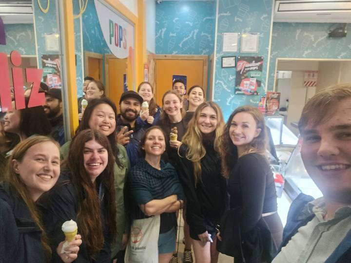 Smiling travelers pose with ice cream cones inside a colorful shop.