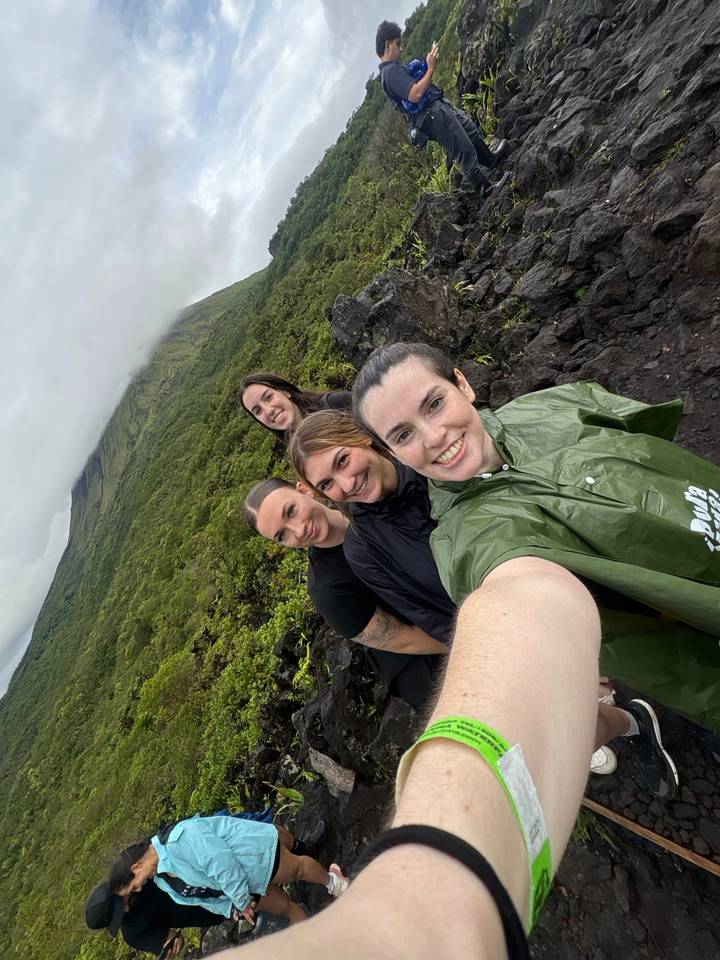 Group selfie during a rainy jungle hike with green ponchos against a foggy hillside.