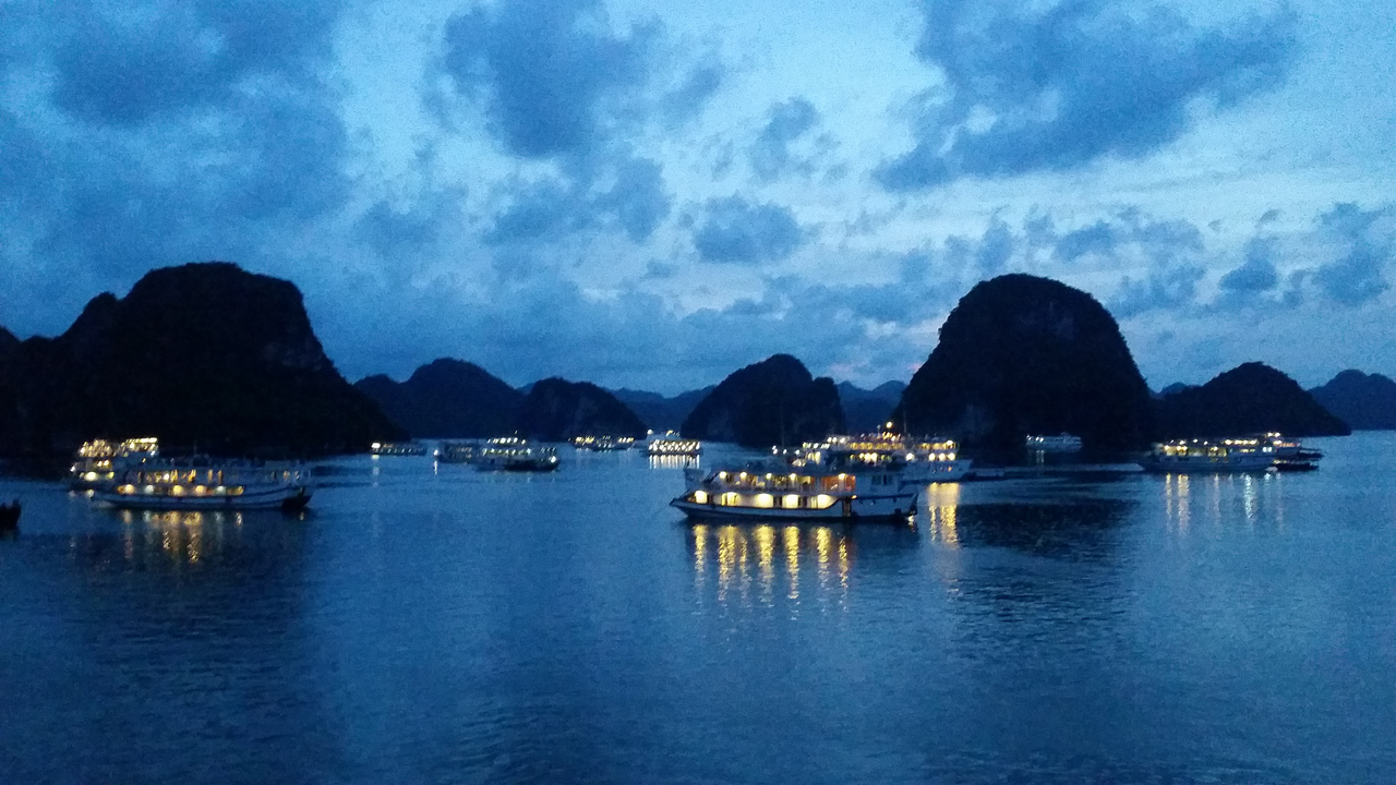 Boats and limestone karsts illuminated at dusk on the water.