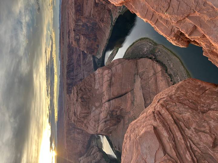 The Colorado River curves around Horseshoe Bend at sunset, viewed from a steep cliff edge.