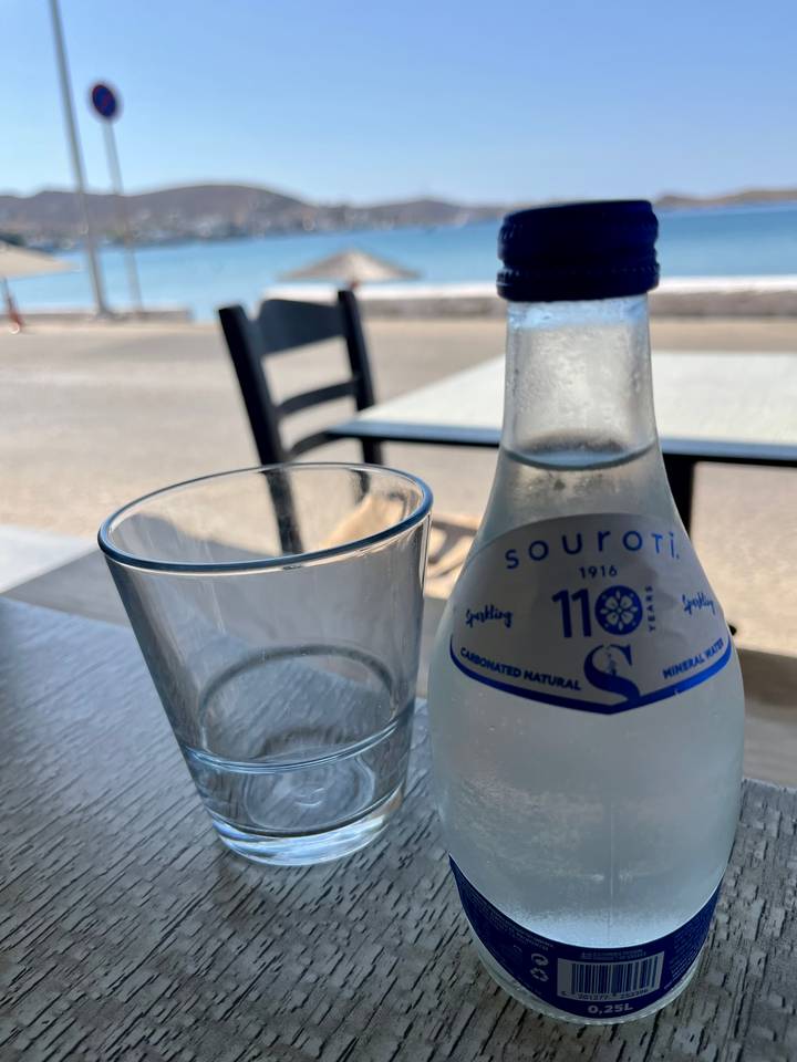 Close-up of a Souroti sparkling water bottle beside an empty glass on an outdoor café table