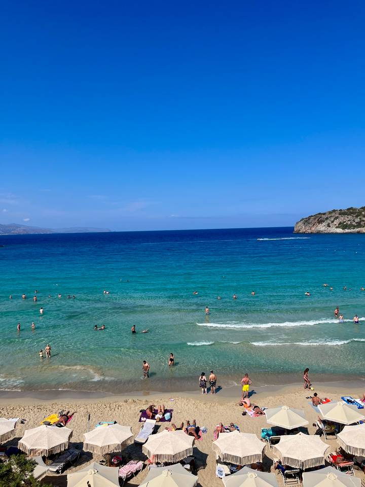 Turquoise Mediterranean beach with dozens of swimmers enjoying clear water below a blue sky