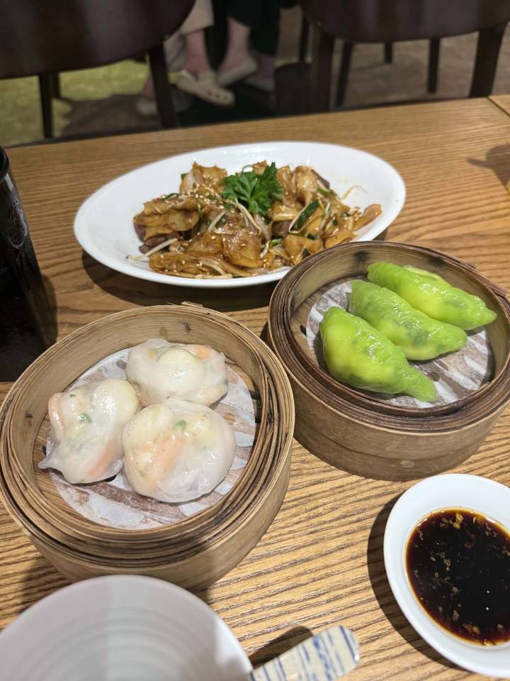 Assortment of dim sum and stir-fried noodles served in bamboo steamers and plates on a wooden table.