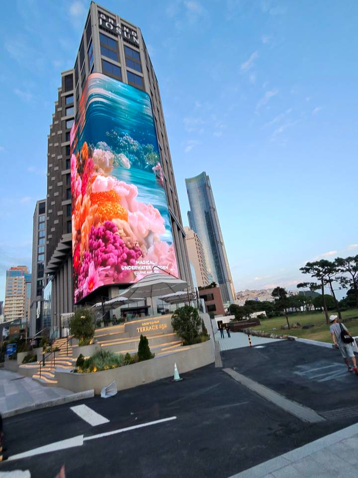 Modern city block in Busan dominated by a towering LED screen displaying vivid underwater imagery.